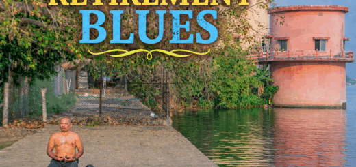 A man sits cross-legged in meditation on a concrete platform beside a calm water body, with trees and a cylindrical building reflected in the water.
