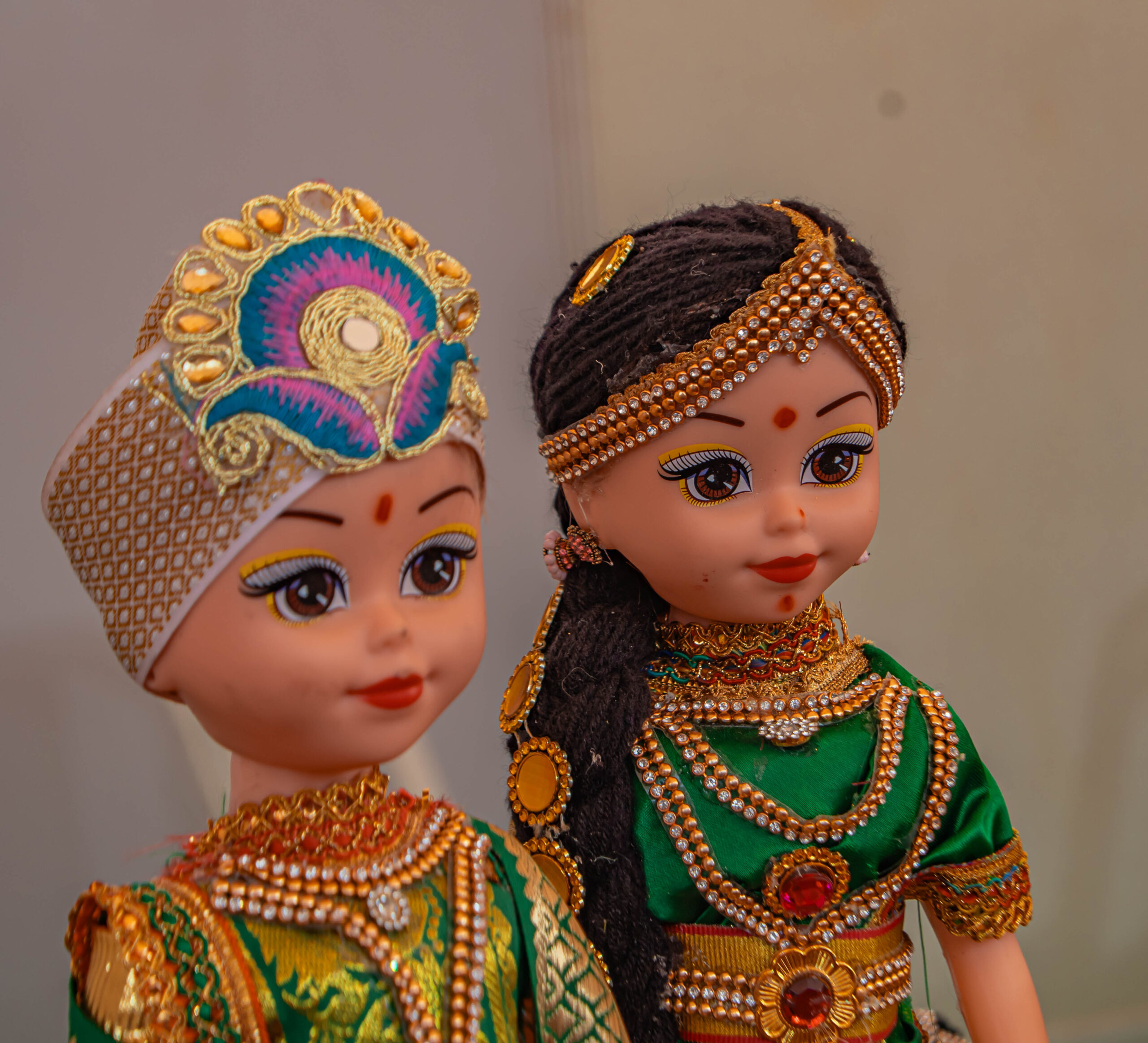Two decorative dolls dressed in traditional Indian attire with jewelry and ornate headpieces.