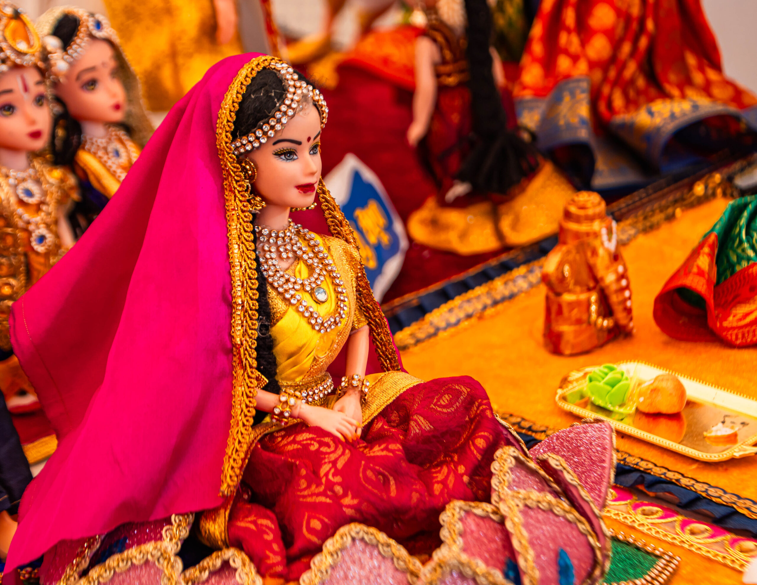 A traditional bride doll dressed in red and gold attire seated among decorative items.